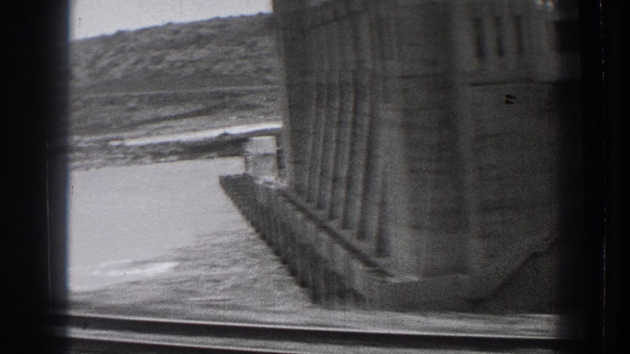1939 Washington 8mm frame with the dam wall seen close at right, water below, and a hillside across the reservoir or river.
