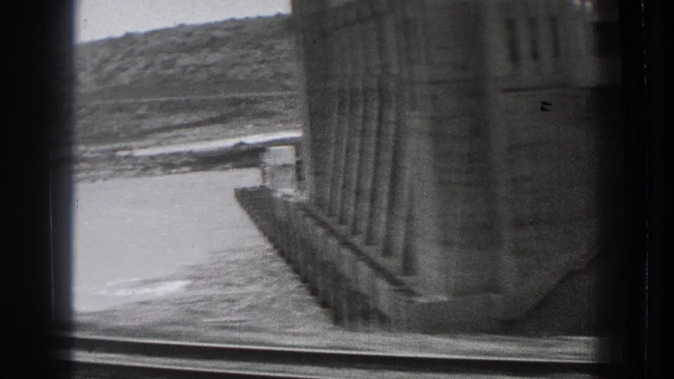 1939 Washington 8mm frame with the dam wall seen close at right, water below, and a hillside across the reservoir or river.