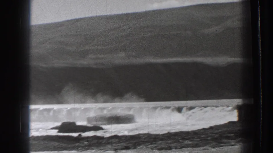 1939 Washington home-movie frame showing rocky waterfront and breaking surf seen through dark train-window framing.