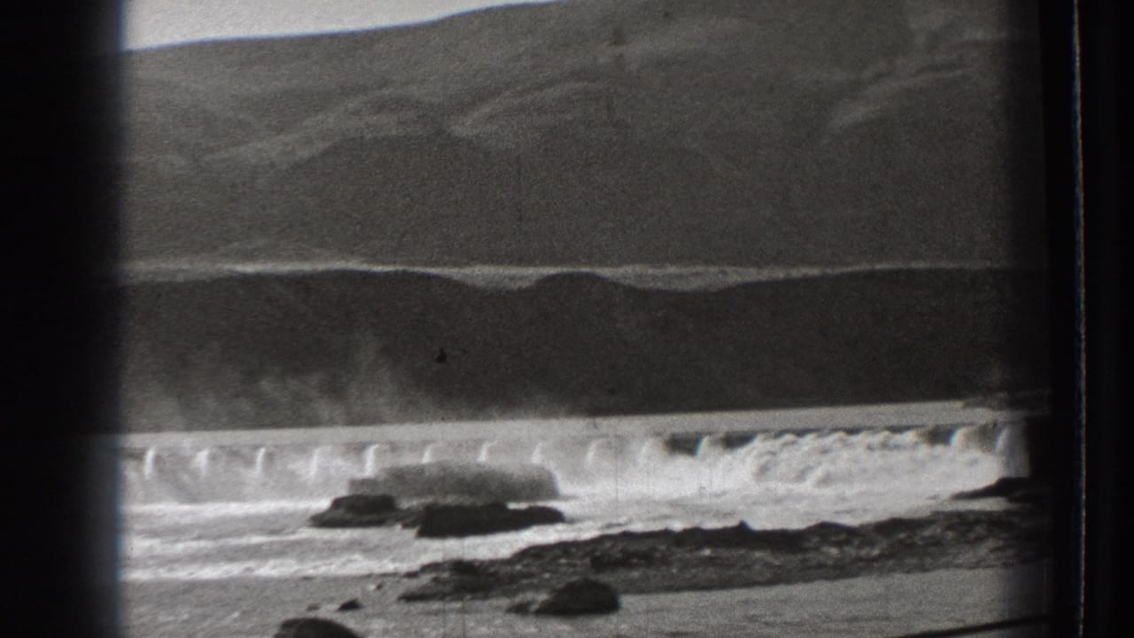 Rocky coast and waves seen through vertical train-window bars.