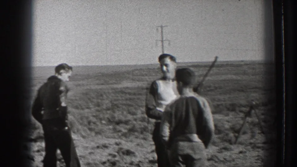 Three men in 1939 Washington home-movie footage stand in open country, with rifles visible and utility poles on the horizon.