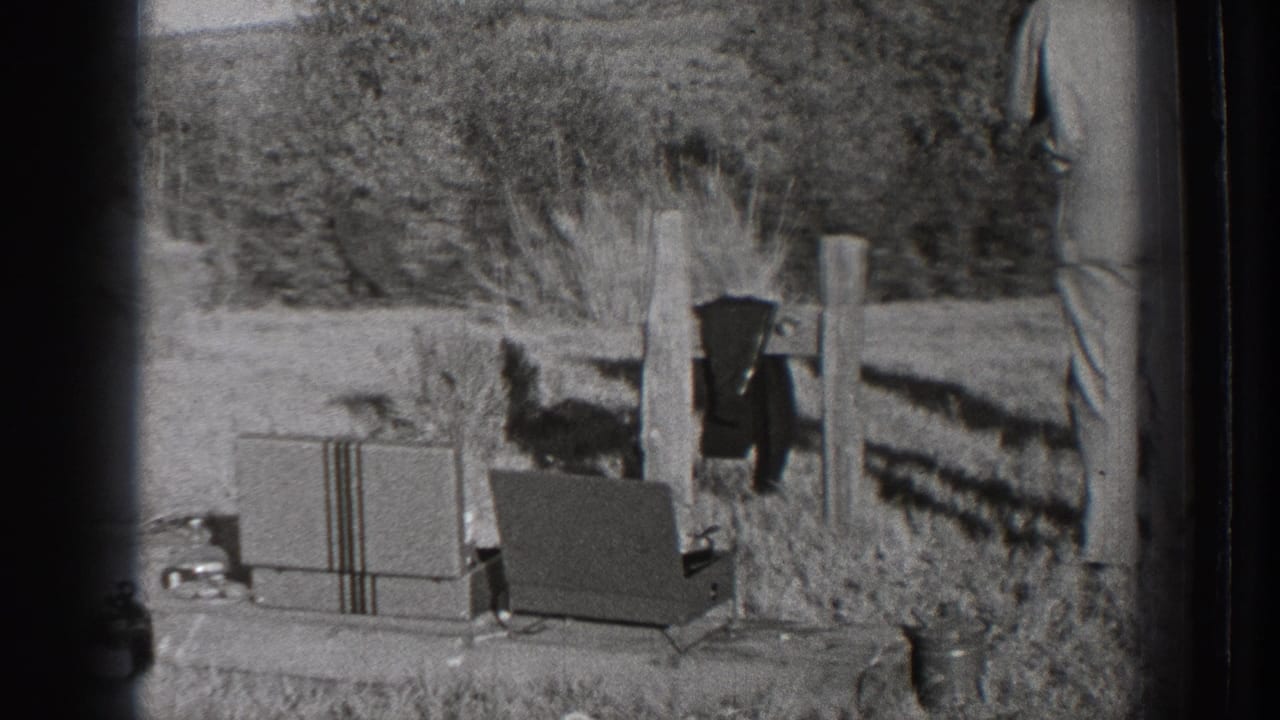 1939 Washington 8mm frame showing a rural field with equipment cases, fence posts, trees, and part of a standing adult man.