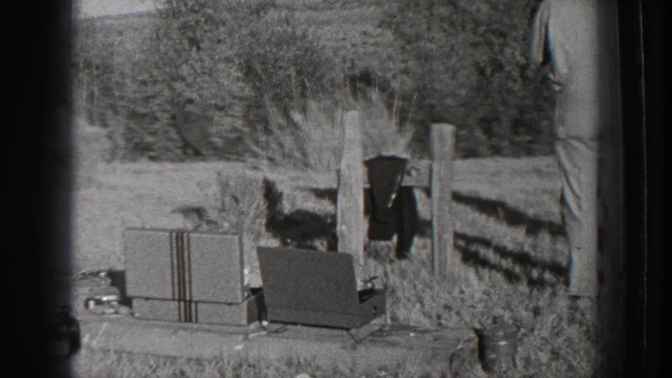 1939 Washington 8mm frame showing a rural field with equipment cases, fence posts, trees, and part of a standing adult man.