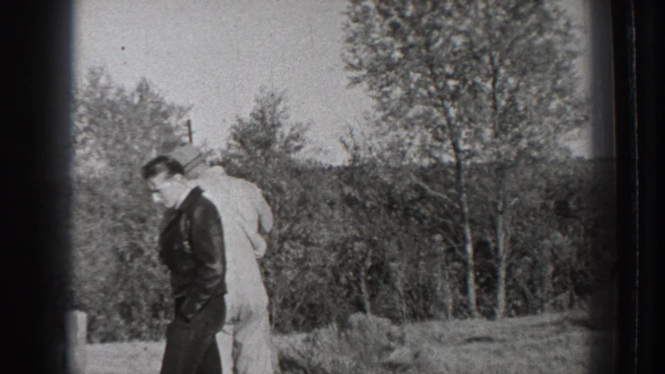 1939 Washington home-movie frame with two adult men in a rural field, one in dark clothing and one in a light suit near trees.