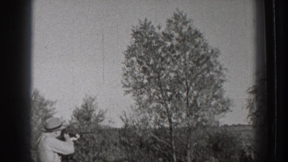 1939 Washington 8mm frame showing an adult man in a light suit and brimmed hat aiming a firearm in an open rural field.