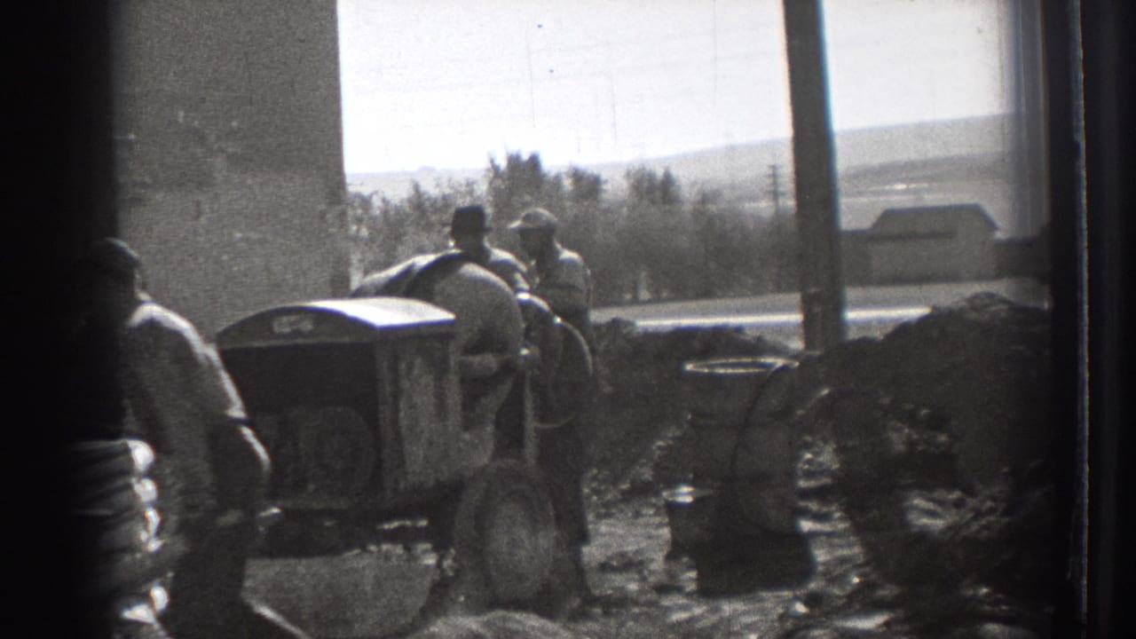 In Washington, 1939, workers gather at a construction site with dirt piles, equipment, and a street visible beyond the building edge.