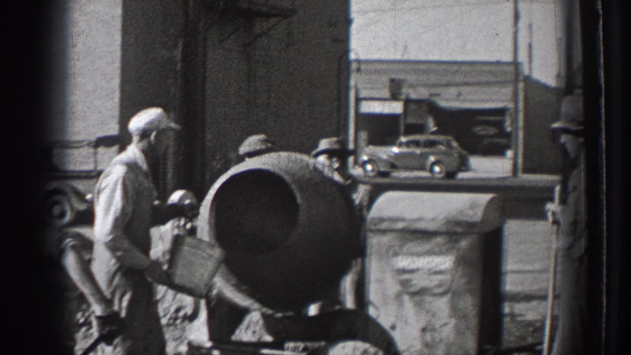Worker handles a bucket beside a cement mixer near a brick wall.