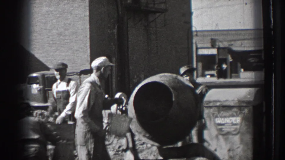 Workers in caps and overalls cluster around a cement mixer at a Washington construction site, with a marked bin and street background visible.