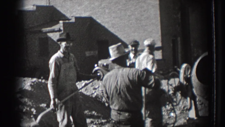 In 1939 Washington footage, adult workers in hats stand near shovels, aggregate, a cement mixer, and a parked vintage car.