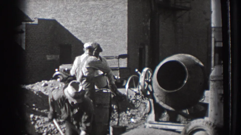 Adult laborers appear to shovel aggregate beside a cement mixer on a Washington construction site, with a 1930s car behind them.