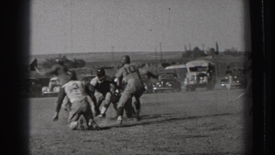 A 1939 Washington football scrimmage moment shows players converging around the ball carrier, with a numbered jersey, dust, spectators, and parked automobiles behind the action.