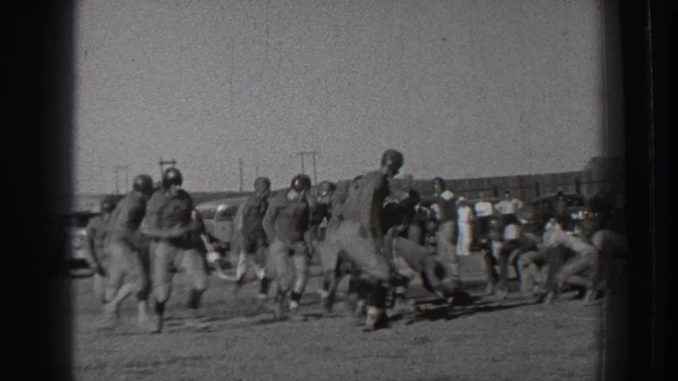 1939 Washington home-movie frame of men in football uniforms and leather-style helmets moving near the line of play on an open field.