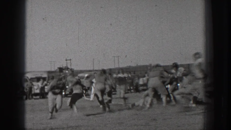 A running football play unfolds on a Washington field in 1939, with uniformed players moving across the frame and spectators behind them.