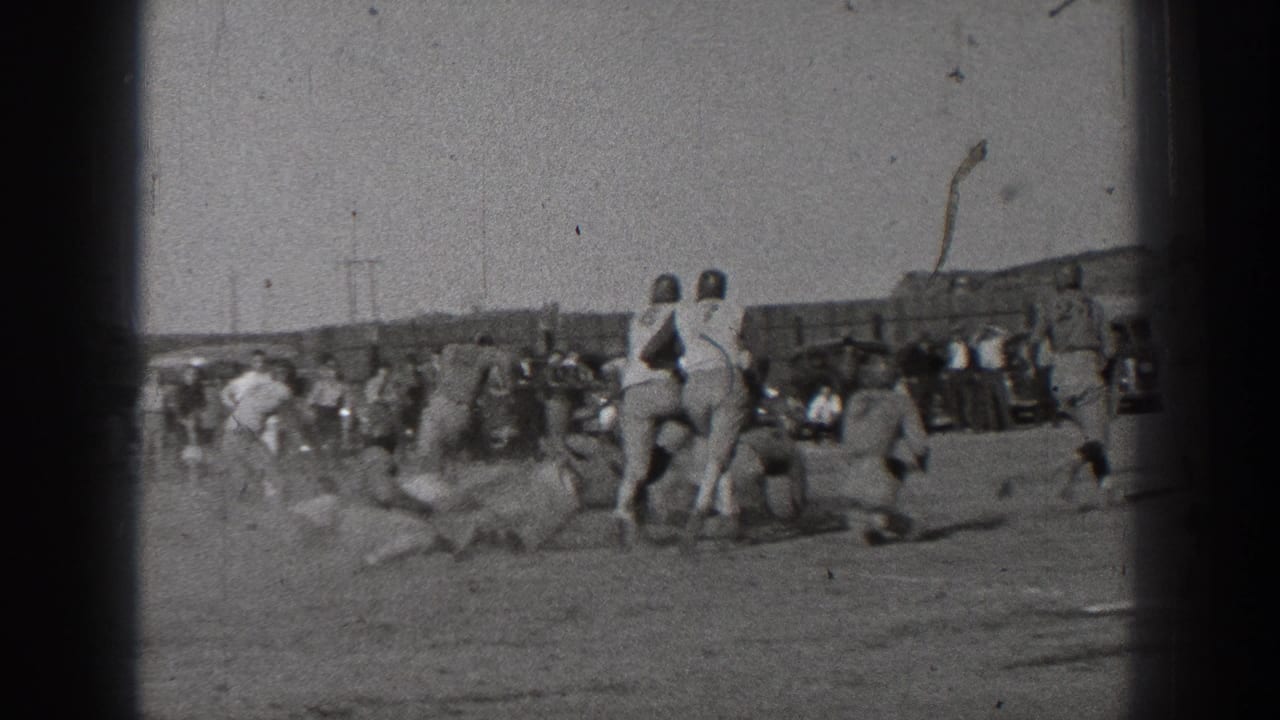 Helmeted football players collide on a dusty field while spectators watch from the sideline.