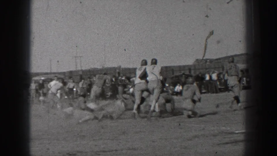 Black-and-white 1939 Washington 8mm footage shows football players in leather-style helmets during a tackle on a dusty field.