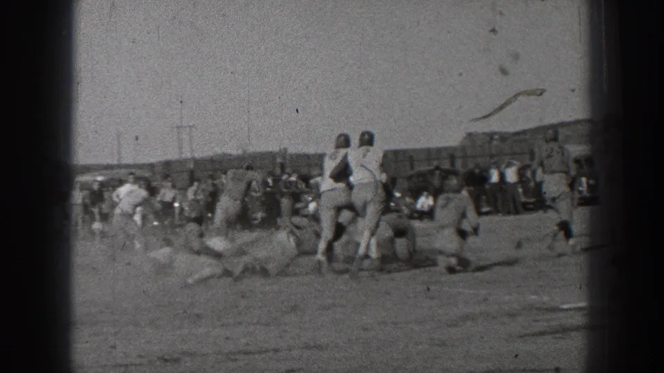 The sideline camera catches a 1939 Washington football play as players gather around a fallen runner on an open dirt field.