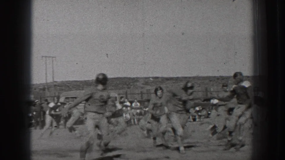 A 1939 Washington football play moves across the frame as helmeted players run on a dusty field before a sideline crowd.