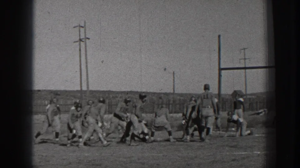 A group of young male football players in helmets gather around the ball on an outdoor Washington field in 1939.