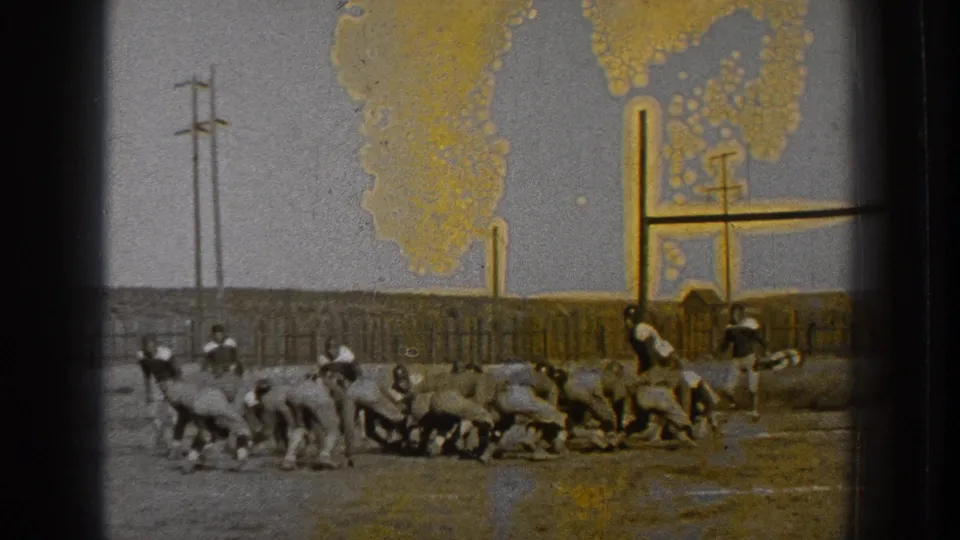 Football players line up low on a field in 1939 Washington, with utility poles, fencing, and color staining on the film frame.