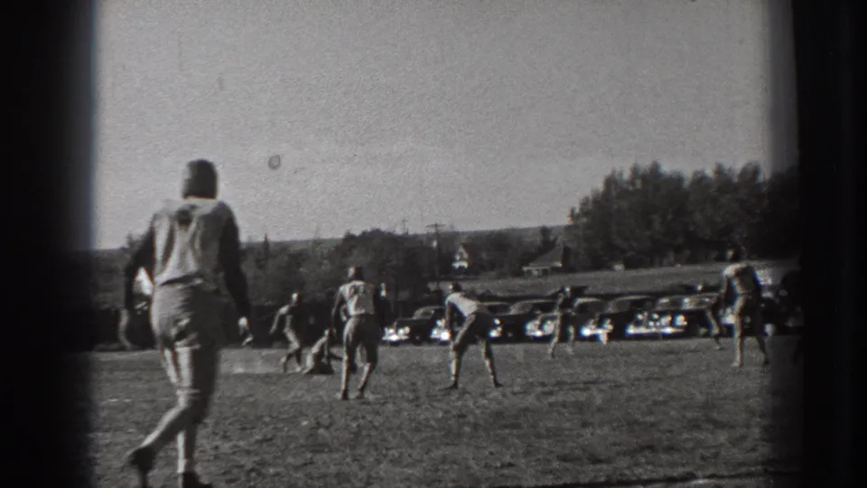 1939 Washington home-movie frame with a spectator or player at the sideline as the football game continues near parked cars.