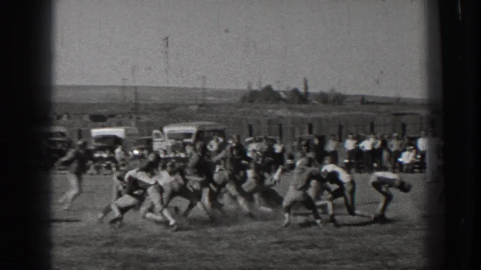 1939 Washington home-movie frame of an amateur football play on an open field, with spectators and parked cars in the background.