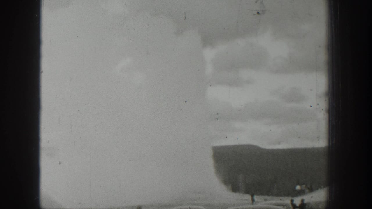 1939 Wyoming home-movie frame with the geyser plume softened by exposure and a few distant people near the lower edge.