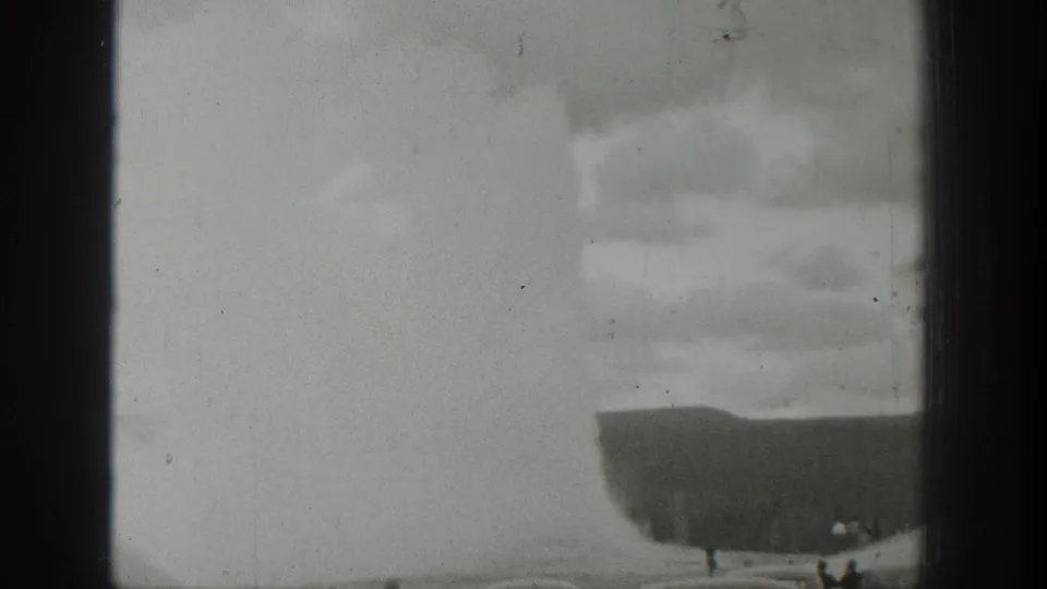 1939 Wyoming home-movie frame with the geyser plume softened by exposure and a few distant people near the lower edge.