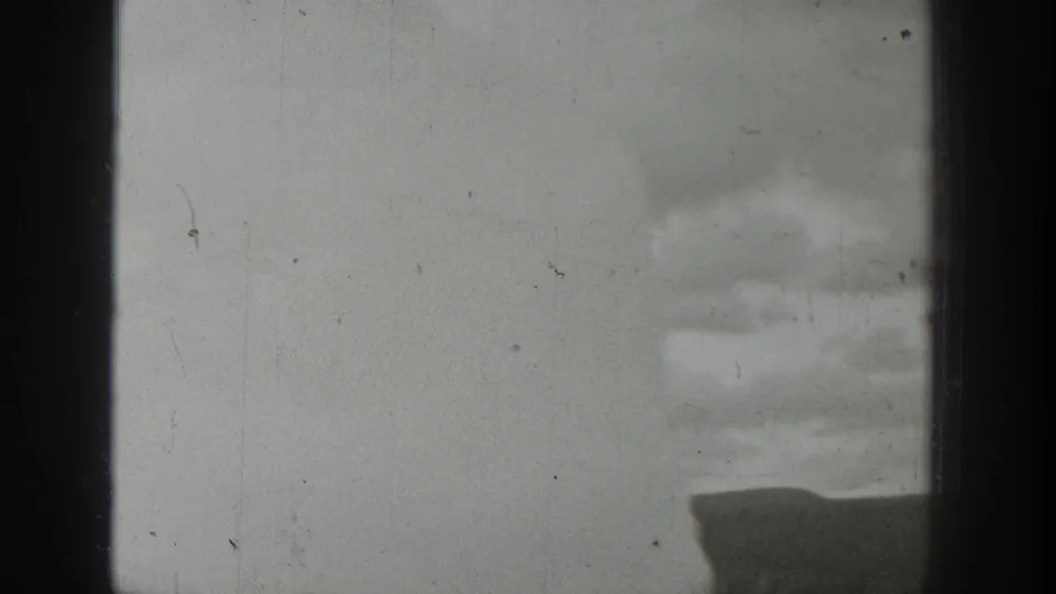 1939 Wyoming frame with steam drifting across a cloudy sky, the geyser basin low in view and tiny spectators barely visible.