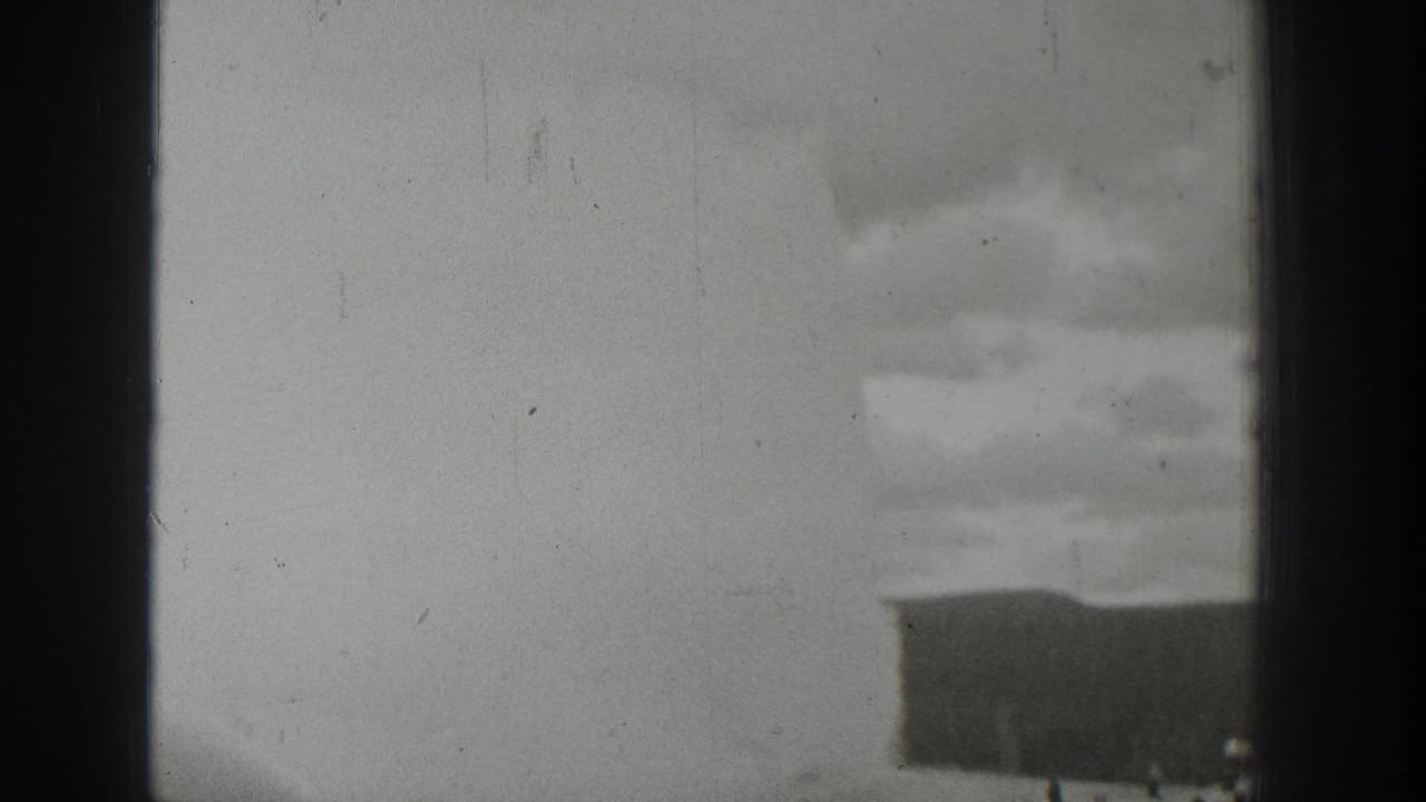 Distant eruption above a dark ridge or structure with tiny people visible near the base.