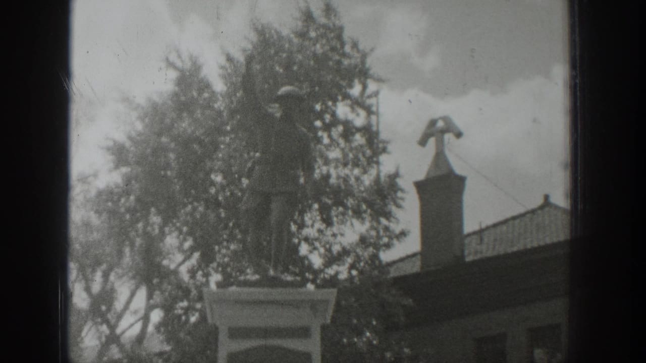Soldier statue on a pedestal near trees and a building roofline.