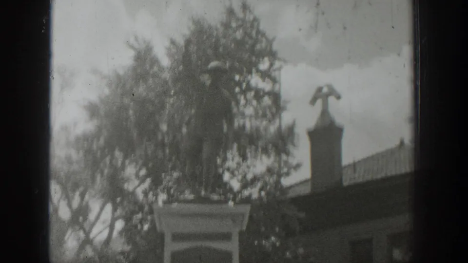 1939 Wyoming 8mm view of the memorial pedestal and surrounding trees, with clouds and a nearby building partly visible.