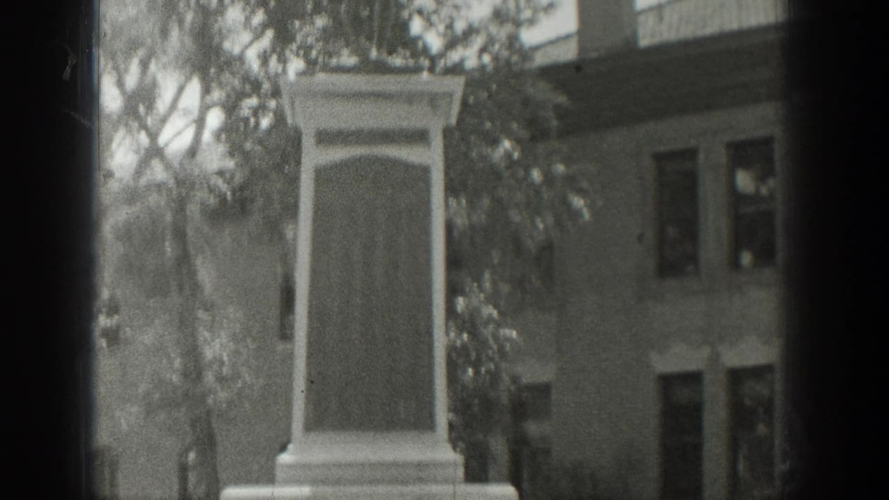 1939 Wyoming 8mm frame showing the upper portion of a stone memorial with trees and an older building behind it.