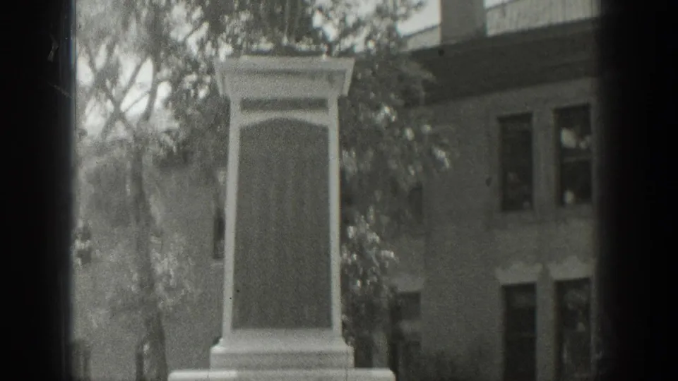 1939 Wyoming 8mm frame showing the upper portion of a stone memorial with trees and an older building behind it.