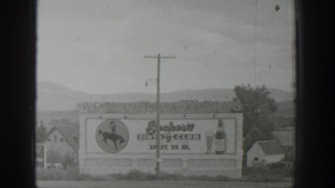 1939 Wyoming 8mm frame showing a roadside dining club and beer billboard with a cowboy logo, bottle graphic, and hills behind it.