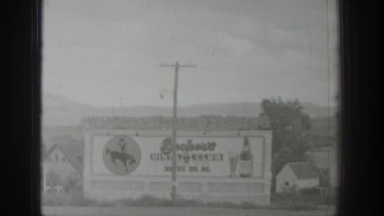 Similar roadside billboard view with hills and a small building behind it.