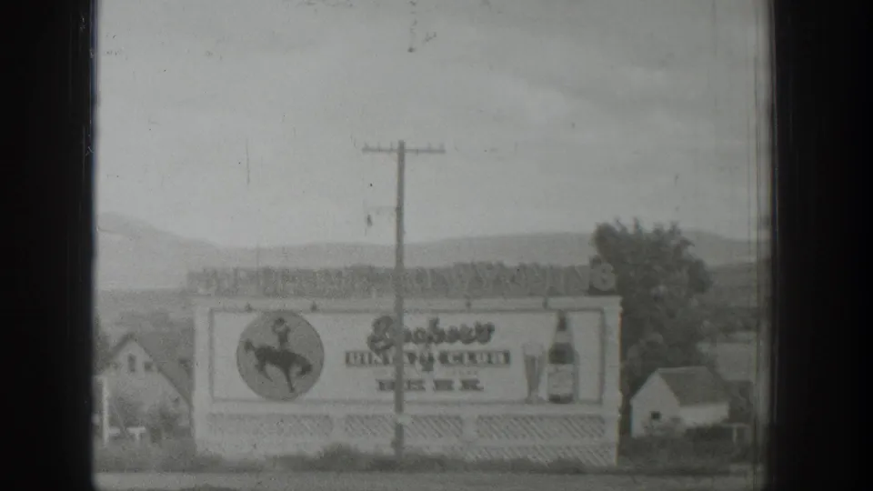 Soft 8mm frame from 1939 Wyoming showing the roadside dining club and beer billboard near small structures and distant hills.