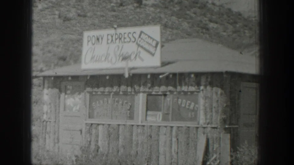 1939 Wyoming 8mm frame showing a rustic roadside food stand with a Pony Express chuck shack sign and scrub-covered hill behind it.