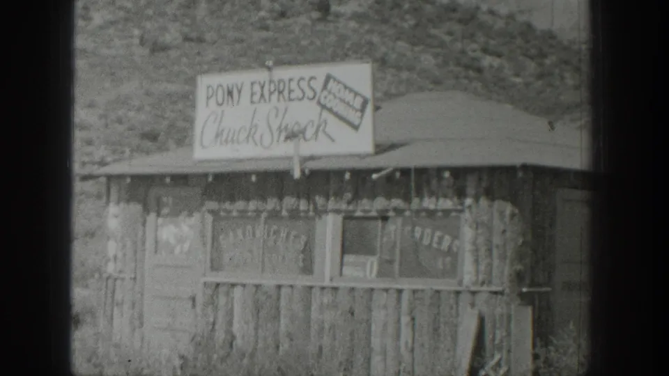 1939 Wyoming 8mm frame showing a weathered roadside food stand with Pony Express Chuck Shack signage and hillside behind it.