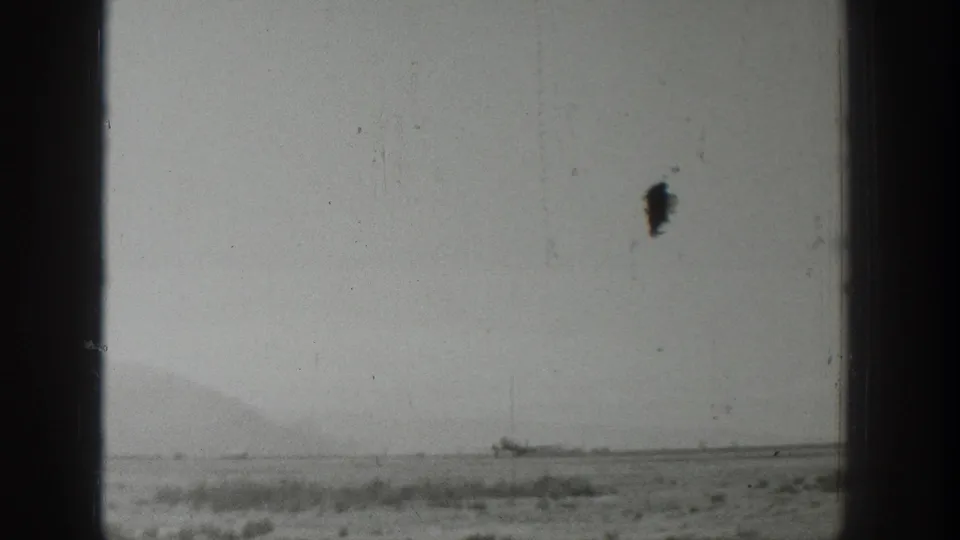 1939 Wyoming 8mm frame shifting from the stand to a hazy open roadside landscape with low hills and a distant object near the horizon.