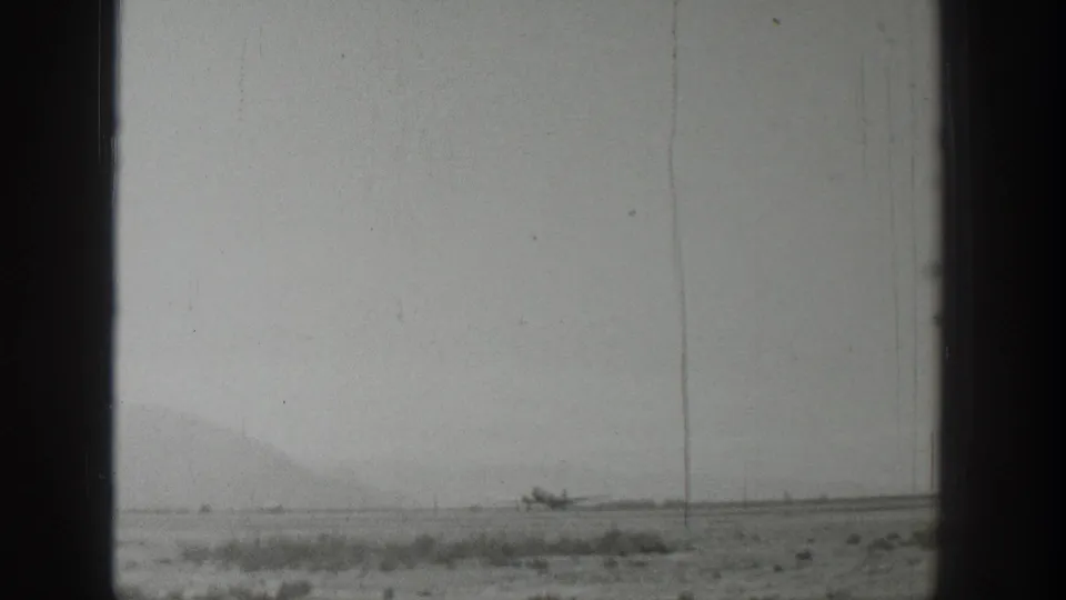 1939 Wyoming home-movie frame showing a broad, pale landscape, low hills, and a small indistinct object on the horizon.