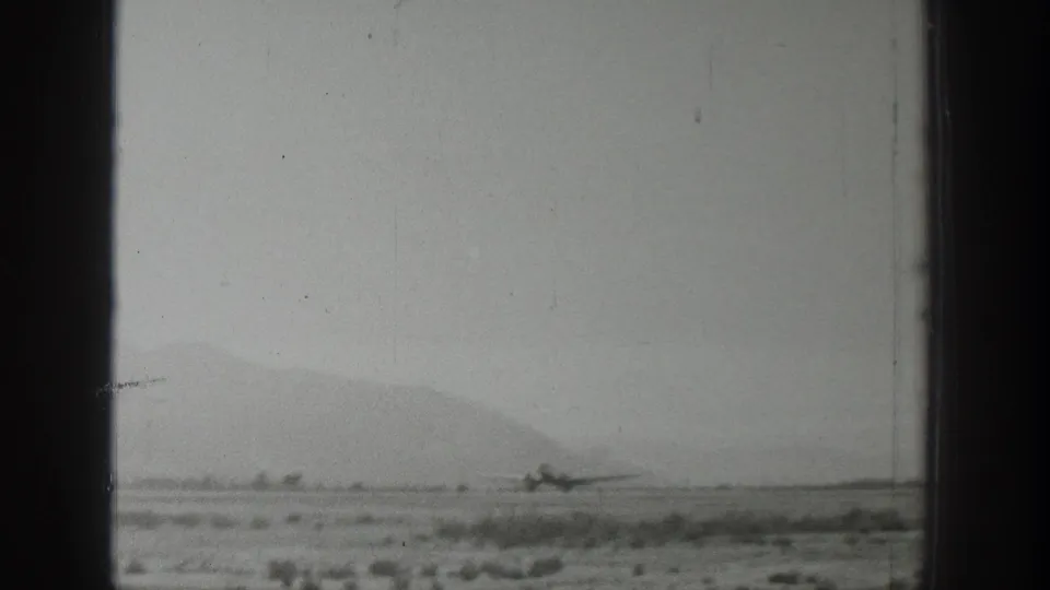 Archival 8mm view of a small airplane on a flat Wyoming runway, partially framed by dark film or window edges and distant hills.