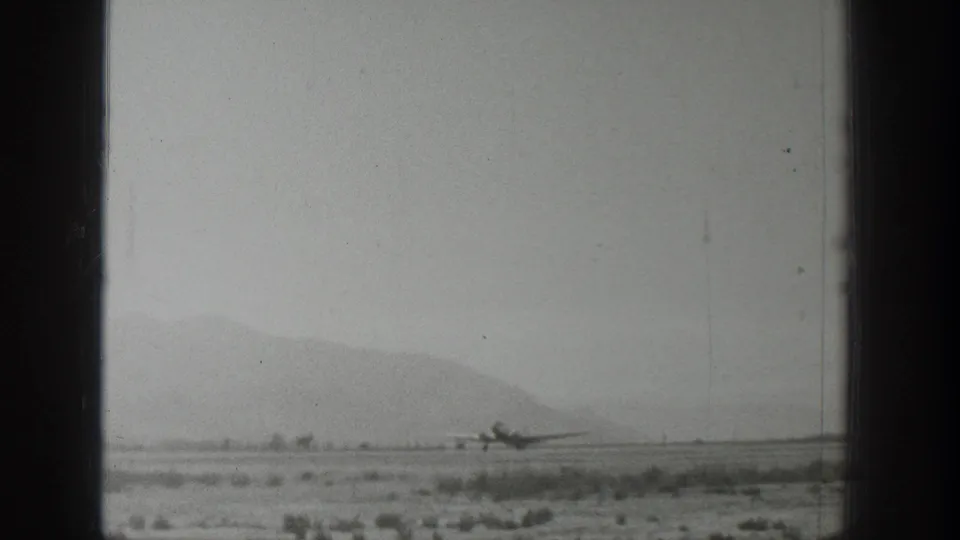Final 1939 Wyoming frame with a small propeller airplane on the runway, scrubby terrain, faint mountains, and aged 8mm film texture.