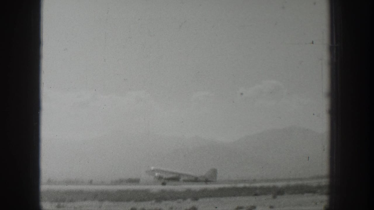 Black-and-white 1939 Wyoming 8mm frame showing a propeller airplane on a runway before distant mountains.