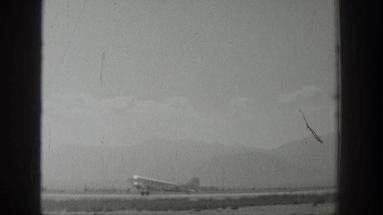 Propeller airplane moving along a runway against a mountain backdrop.