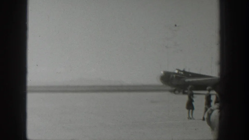Black-and-white 1939 Wyoming 8mm frame showing a propeller airplane near pedestrians on an open runway area.