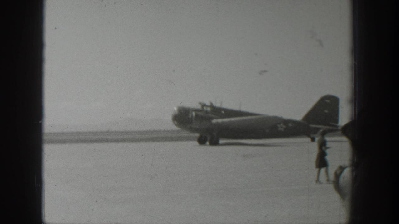 Military-marked propeller aircraft on a runway with a person walking nearby.