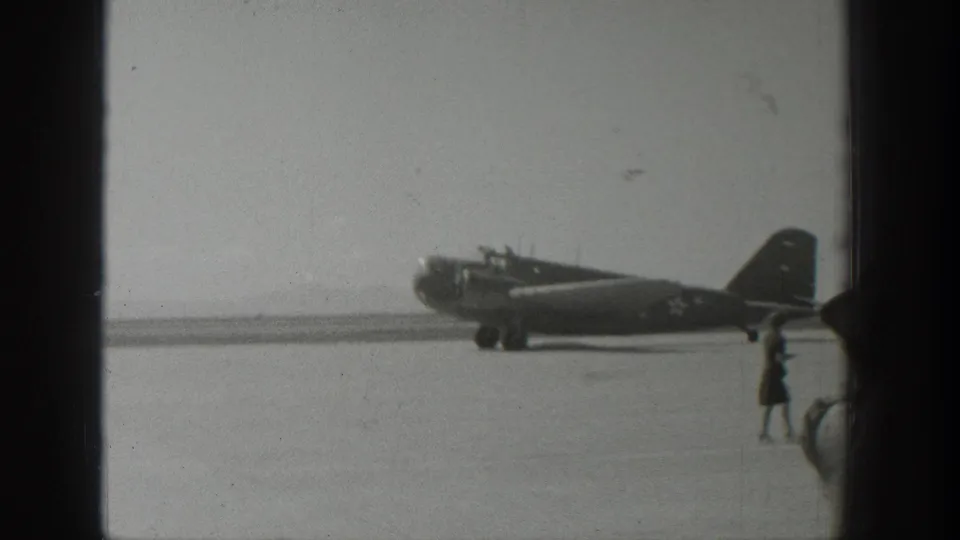1939 Wyoming 8mm frame showing a propeller aircraft with U.S. star insignia on a runway as a distant person walks near the tail area.