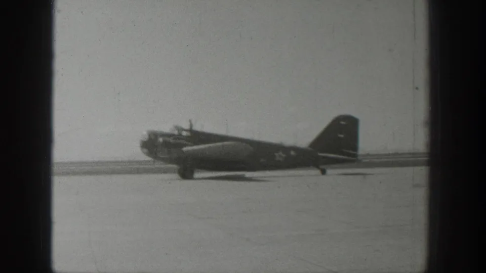 1939 Wyoming 8mm frame showing a military-marked propeller aircraft on a flat airport runway, viewed through dark film-edge obstructions.