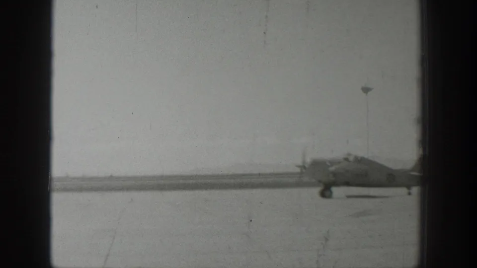 1939 Wyoming 8mm frame showing the same propeller aircraft farther across the runway, partly softened by exposure and film wear.