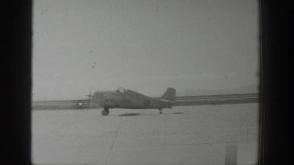 1939 Wyoming 8mm frame showing a propeller aircraft on the runway in a distant side view, with soft focus and visible film texture.